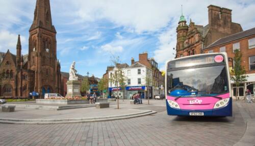 Autobus in arrivo a Church Place, Dumfries, con la statua di Robert Burns e la Greyfriars Kirk sullo sfondo