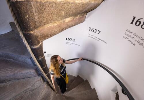 A woman climbs the spiral steps, reading the timeline painted onto the walls